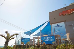 A building with a large fish sculpture on the facade and a banner advertising 'Fish & Chips' and 'Coffee & Cool Drinks'.