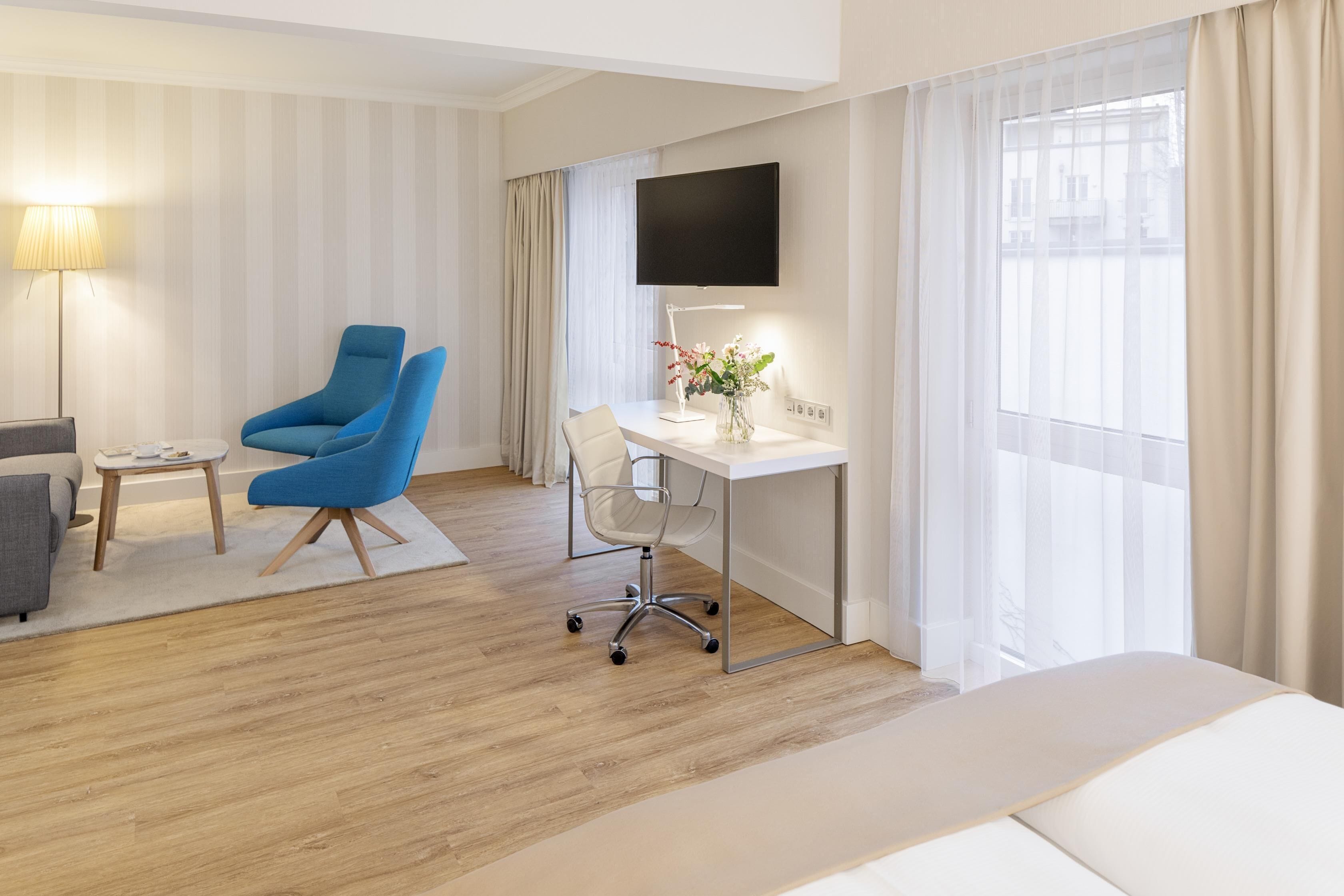 Ein Hotelzimmer mit einem Bett, einem Schreibtisch mit Stuhl, einem Fernseher und einem Fenster mit Vorhängen.