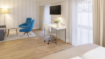 Ein Hotelzimmer mit einem Bett, einem Schreibtisch mit Stuhl, einem Fernseher und einem Fenster mit Vorhängen.