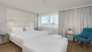 Habitació d'hotel amb un llit gran, una taula auxiliar, un butaques blau i vistes a l'exterior per la finestra.