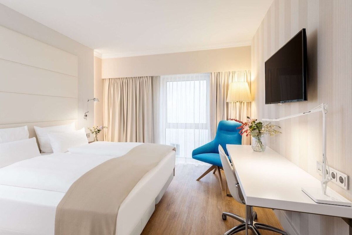 A hotel room with a large bed, a desk, a chair, a TV, and a window with curtains.