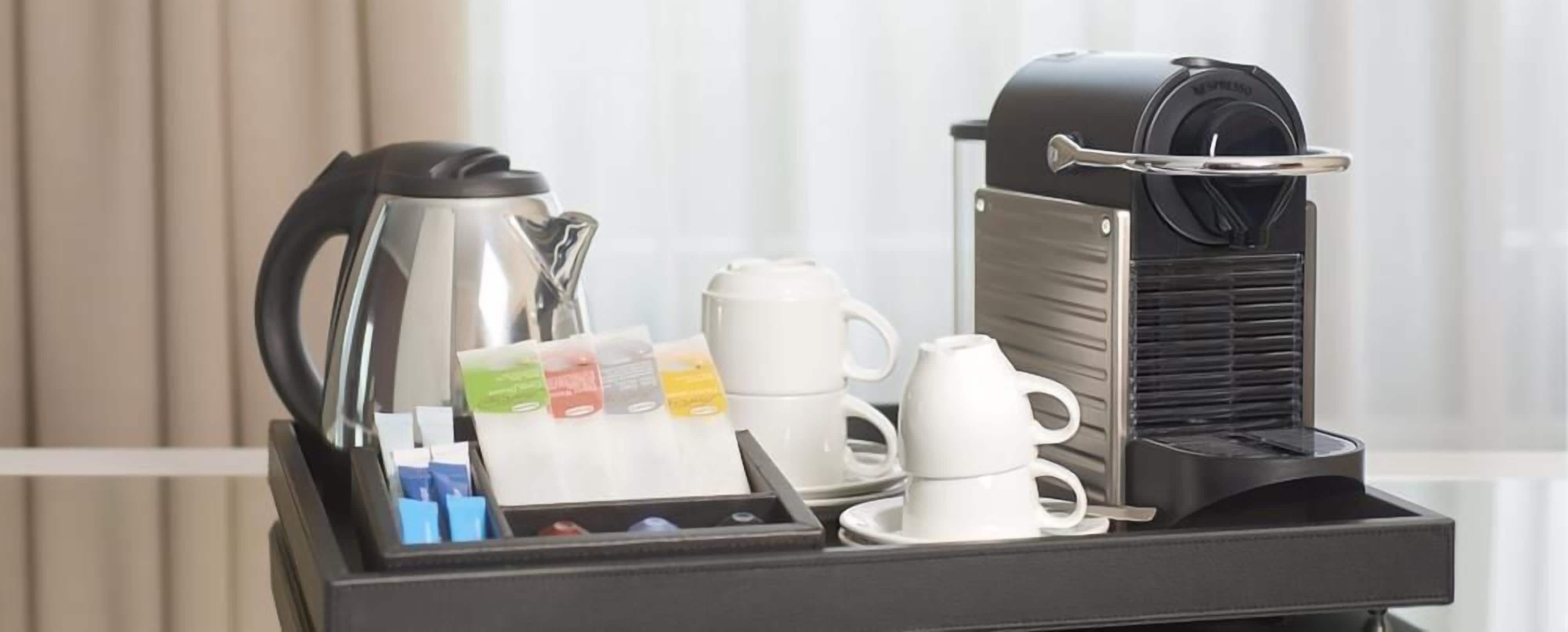Eine Kaffeestation mit Kaffeemaschine, Wasserkocher, Tassen und einer Ablage mit Kaffeekapseln und einem Löffel.