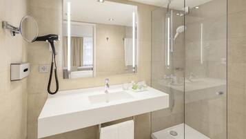 Un baño moderno con un espejo grande, un secador de pelo, un lavamanos y una ducha con mampara de vidrio.