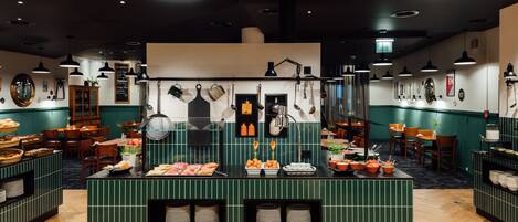 A restaurant with a central island featuring food displays, hanging kitchen utensils, and a chalkboard menu.