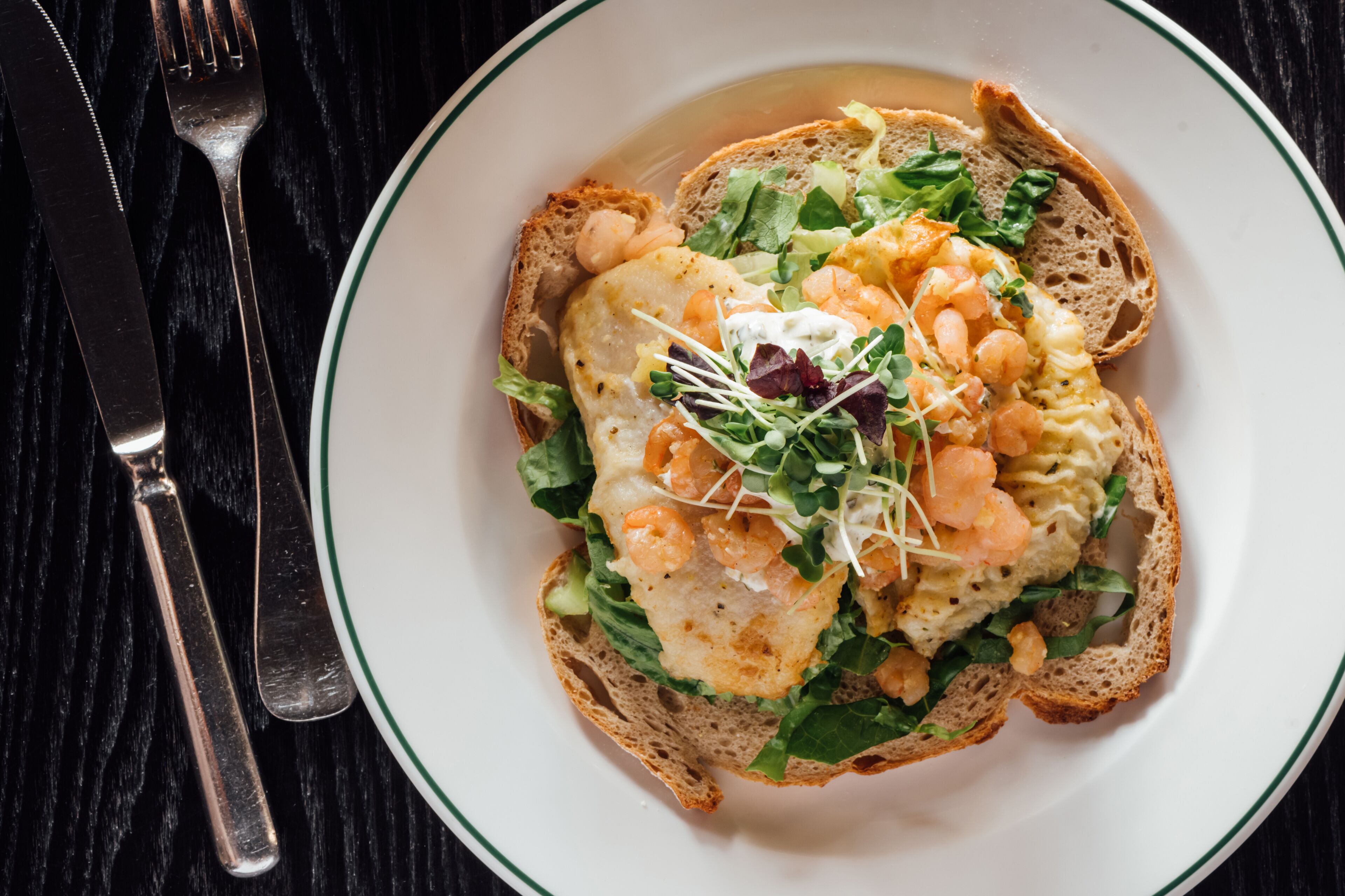 A plate of food with shrimp, greens, and a poached egg on toast.
