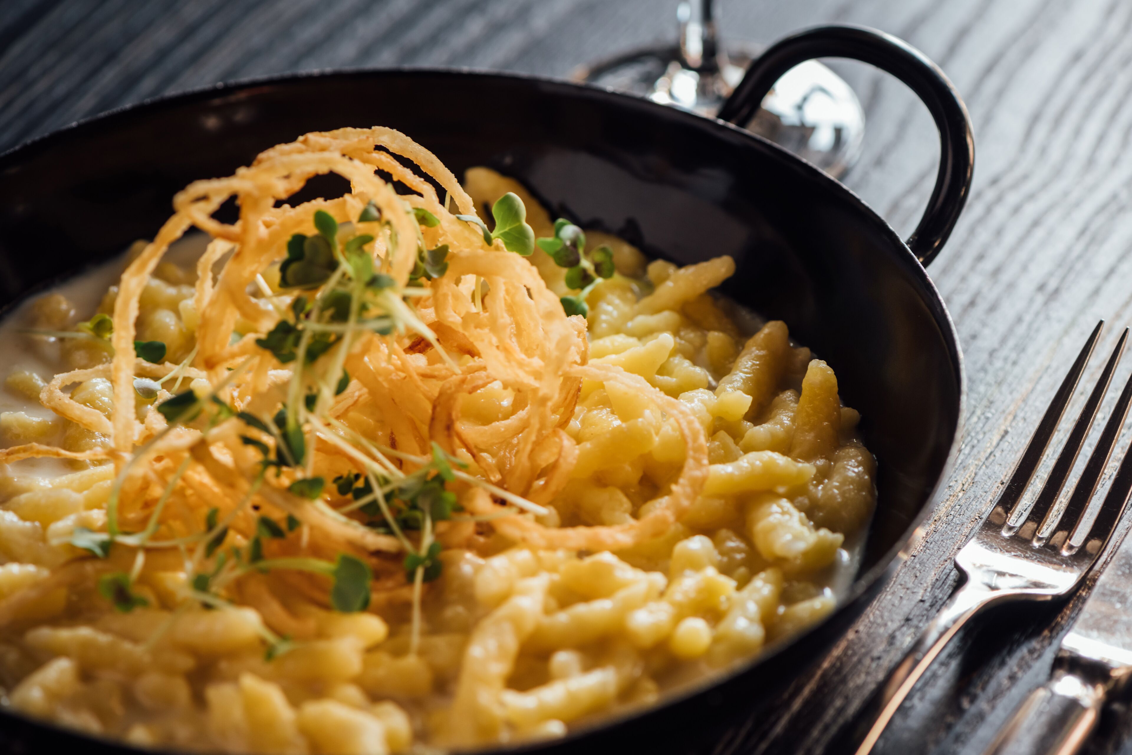 A bowl of macaroni and cheese garnished with crispy onions and herbs.