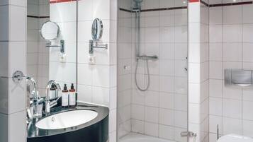 Un baño moderno con un lavamanos negro, azulejos blancos, una ducha con cerramiento de vidrio y un inodoro.