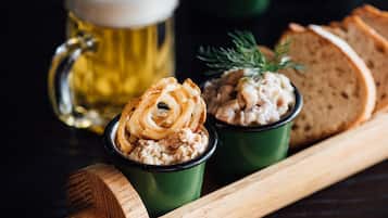 A wooden serving board with two green cups containing food, a beer mug, and slices of bread.