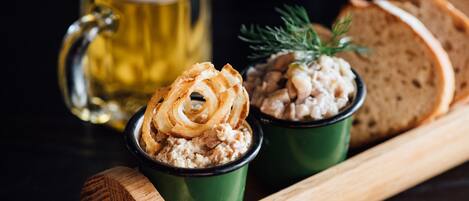 A wooden serving board with two green cups containing food, a beer mug, and slices of bread.