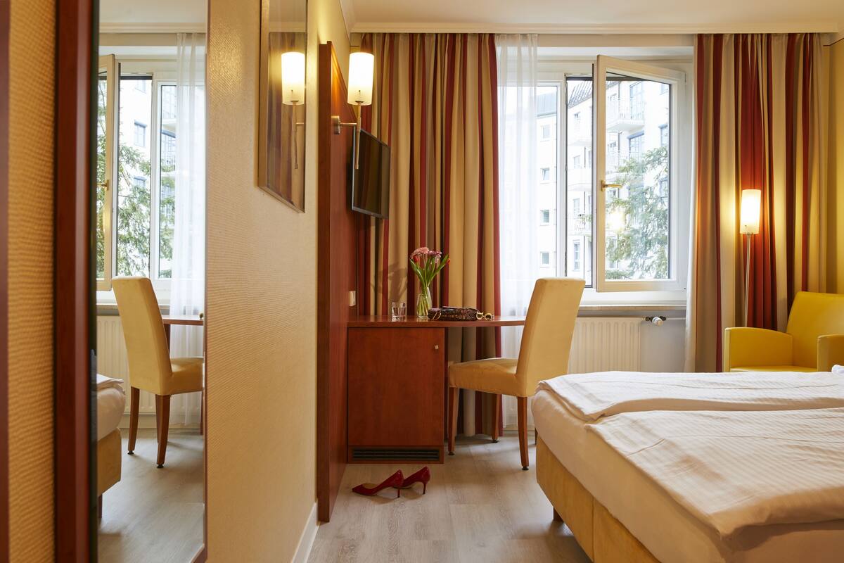 A hotel room with a bed, a desk with a chair, a TV, and a window with curtains.
