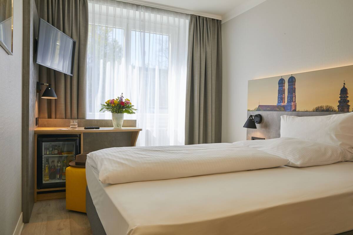 A hotel room with a bed, a desk with a computer, a TV, and a small fridge.