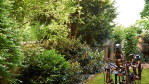 A garden with a metal sculpture of figures seated at a table. - Hotel Concorde München (Munich)