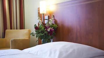 Habitación de hotel con cama, una silla, lámpara de pared y un florero con flores.