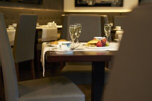 A dining table set with a plate of fruit, two glasses of water, and a cup.