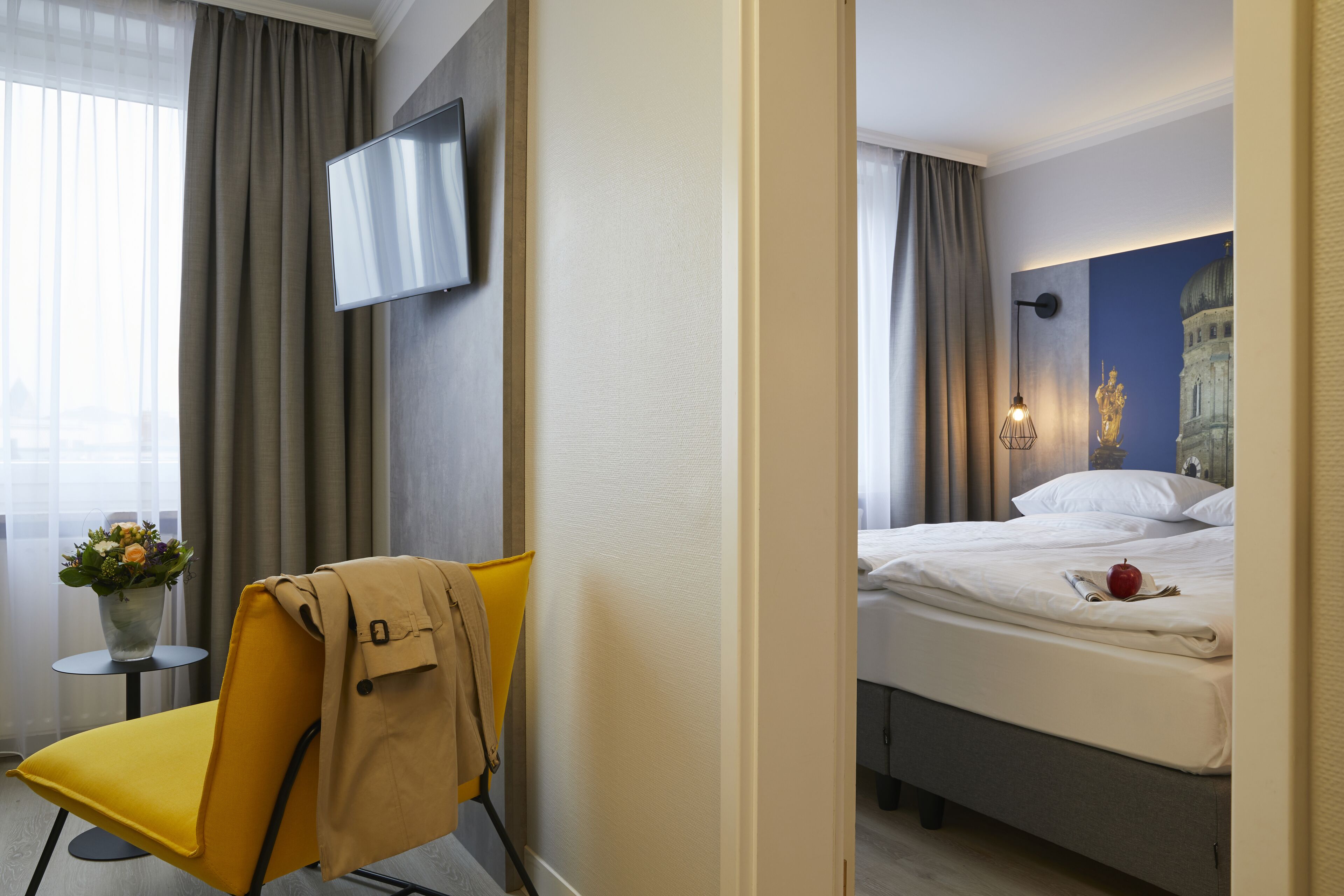 A hotel room with a bed, a chair, a TV, and a painting on the wall.