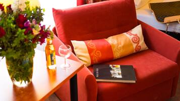 A red sofa with a patterned pillow, a book, a glass of wine, and a vase of flowers on a wooden side table.