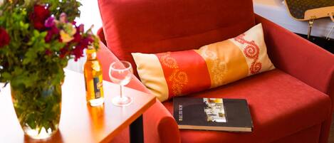 Un sofá rojo con un cojín estampado, un libro, una copa de vino y un florero sobre una mesita de madera.
