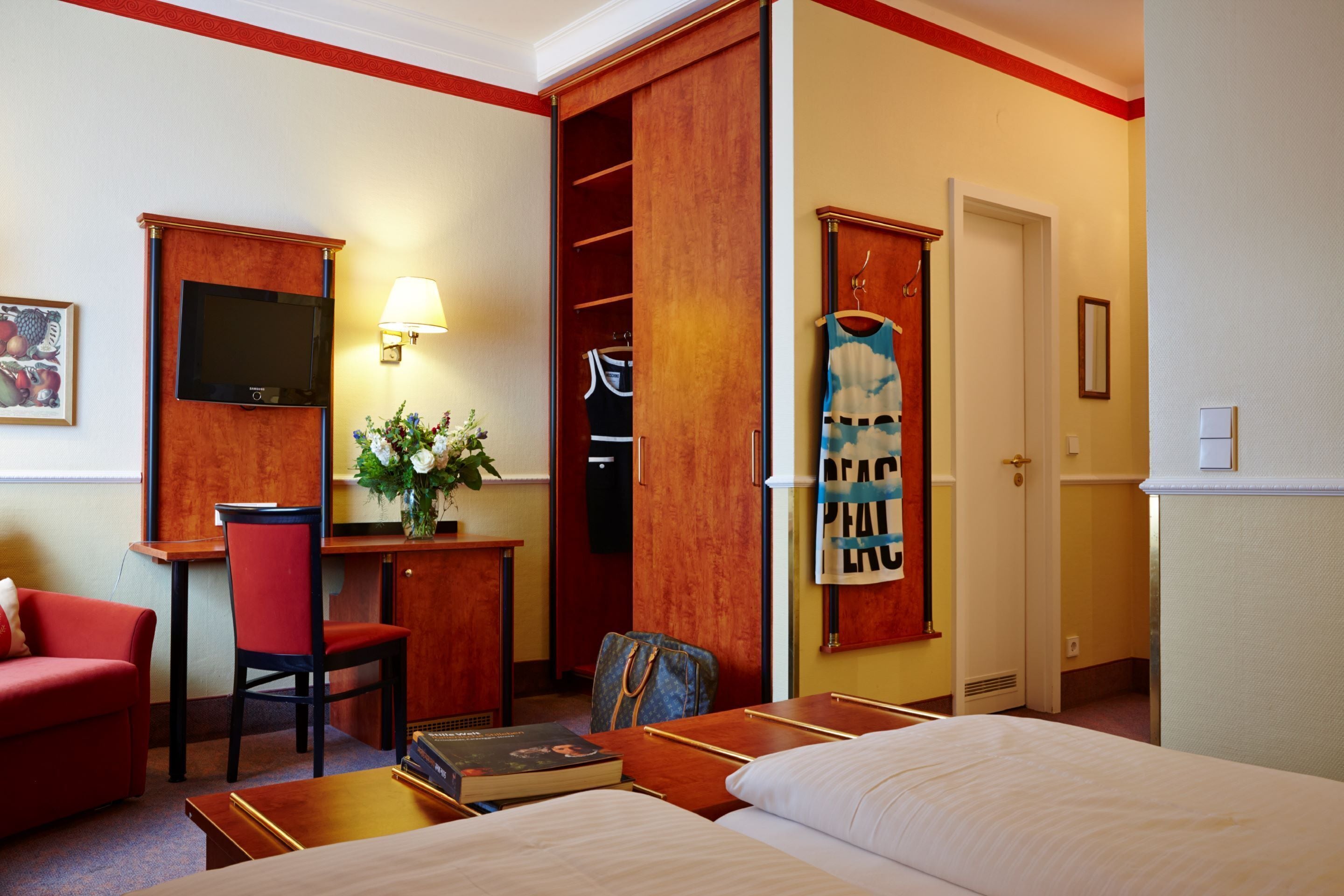 Ein Hotelzimmer mit Bett, Schreibtisch mit Stuhl, Fernseher, Kleiderschrank und Wandlampe.