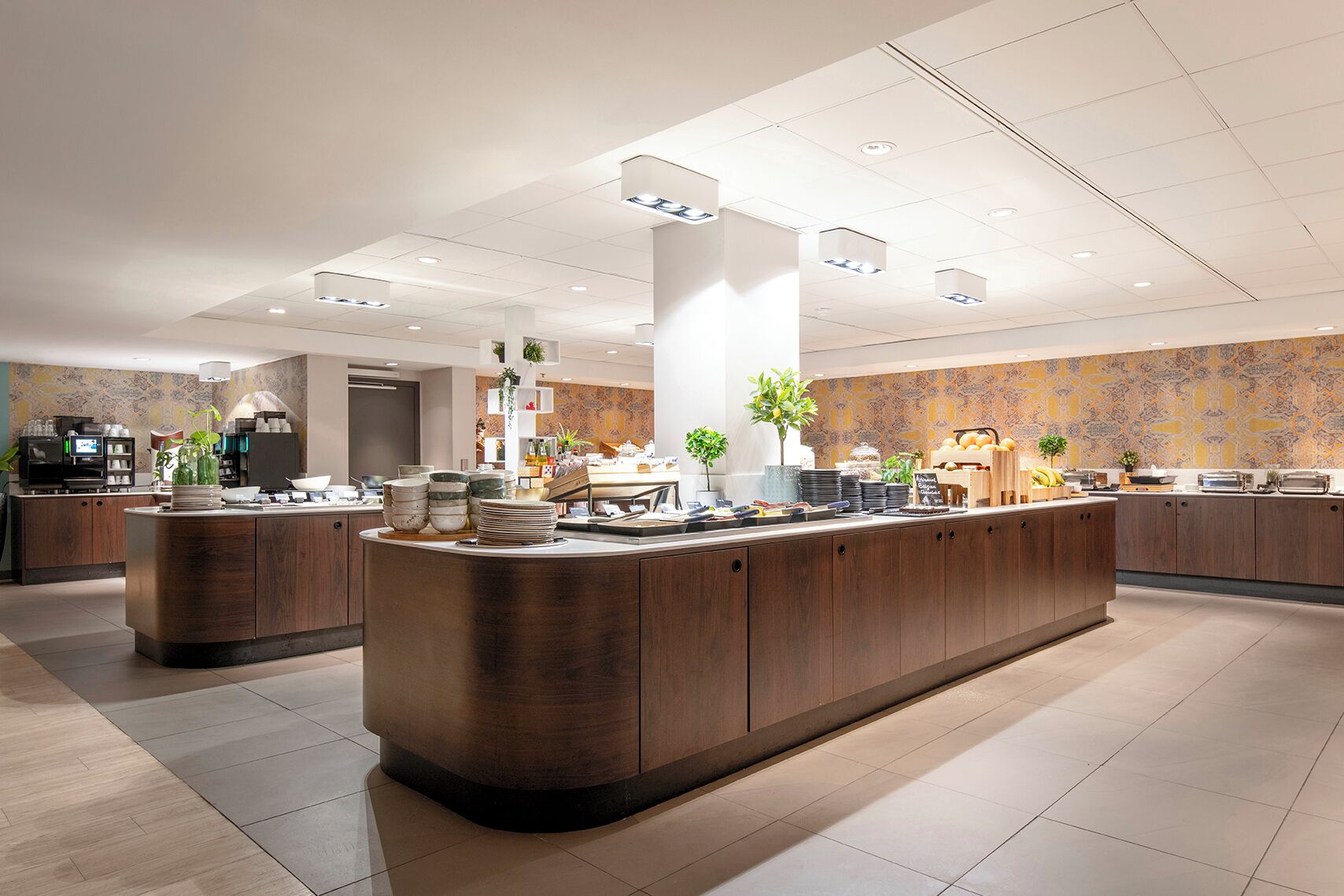 A modern hotel lobby with a central reception desk, a coffee station, and a decorative wall with a patterned design.