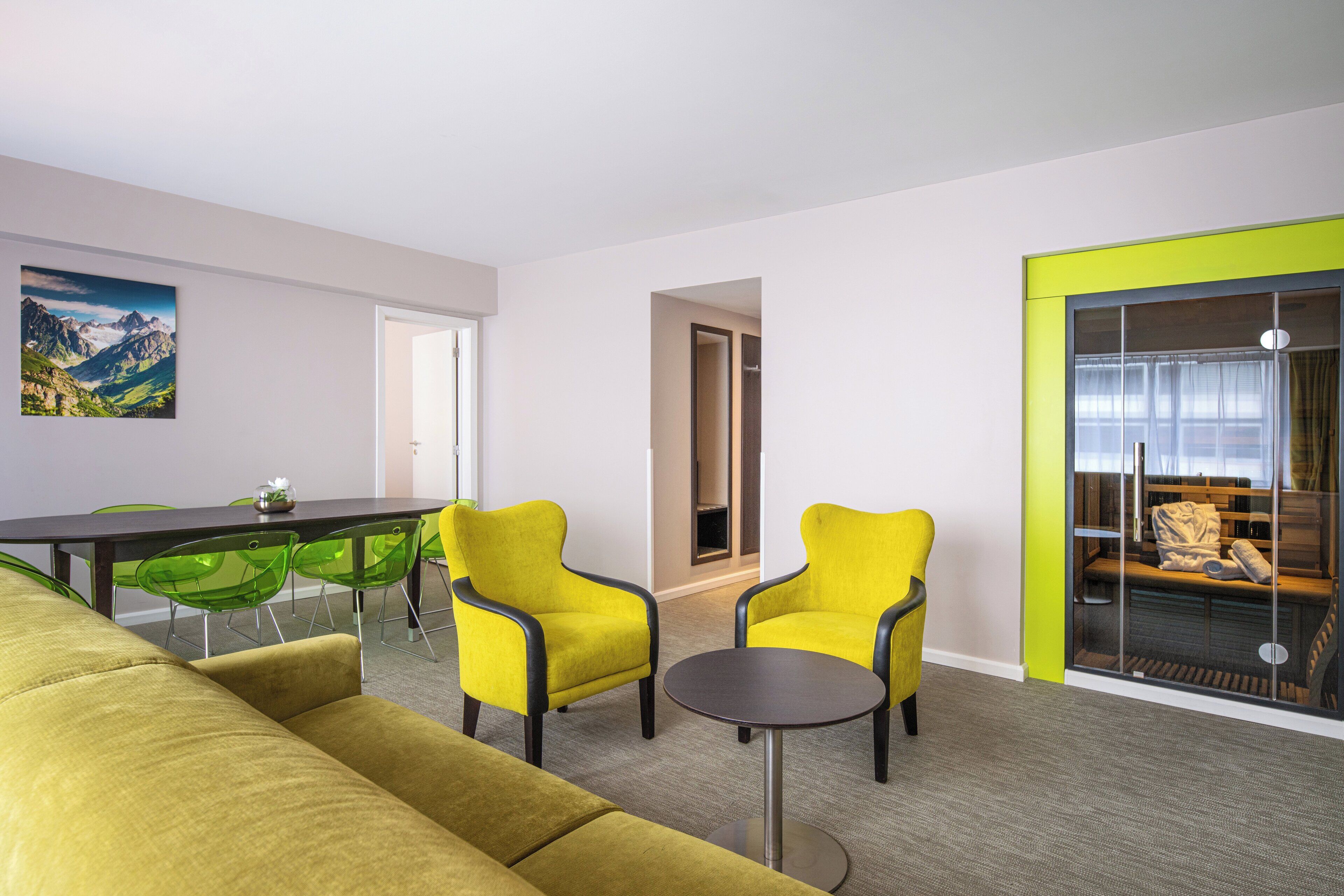 Un salon moderne avec un canapé, deux fauteuils jaunes, une table ronde et un coin repas comprenant une table et des chaises.