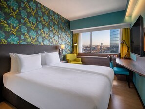 Una habitación de hotel con una cama grande, un escritorio, una silla y vistas a la ciudad.