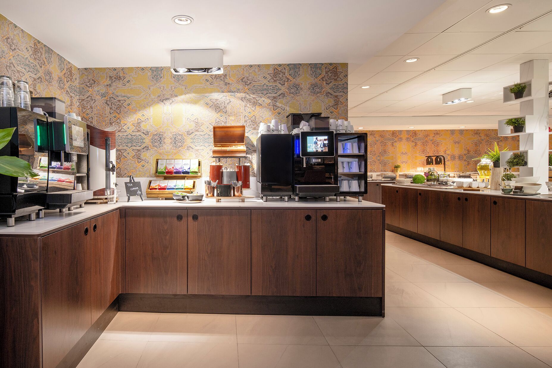 A modern coffee shop with a central island counter, espresso machines, and a television screen.
