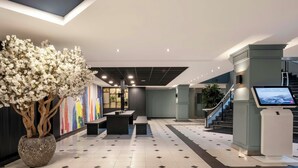 A spacious lobby with a large potted tree, a reception desk, a staircase, and a digital information kiosk. - Thon Hotel Brussels City Centre (Brussels)