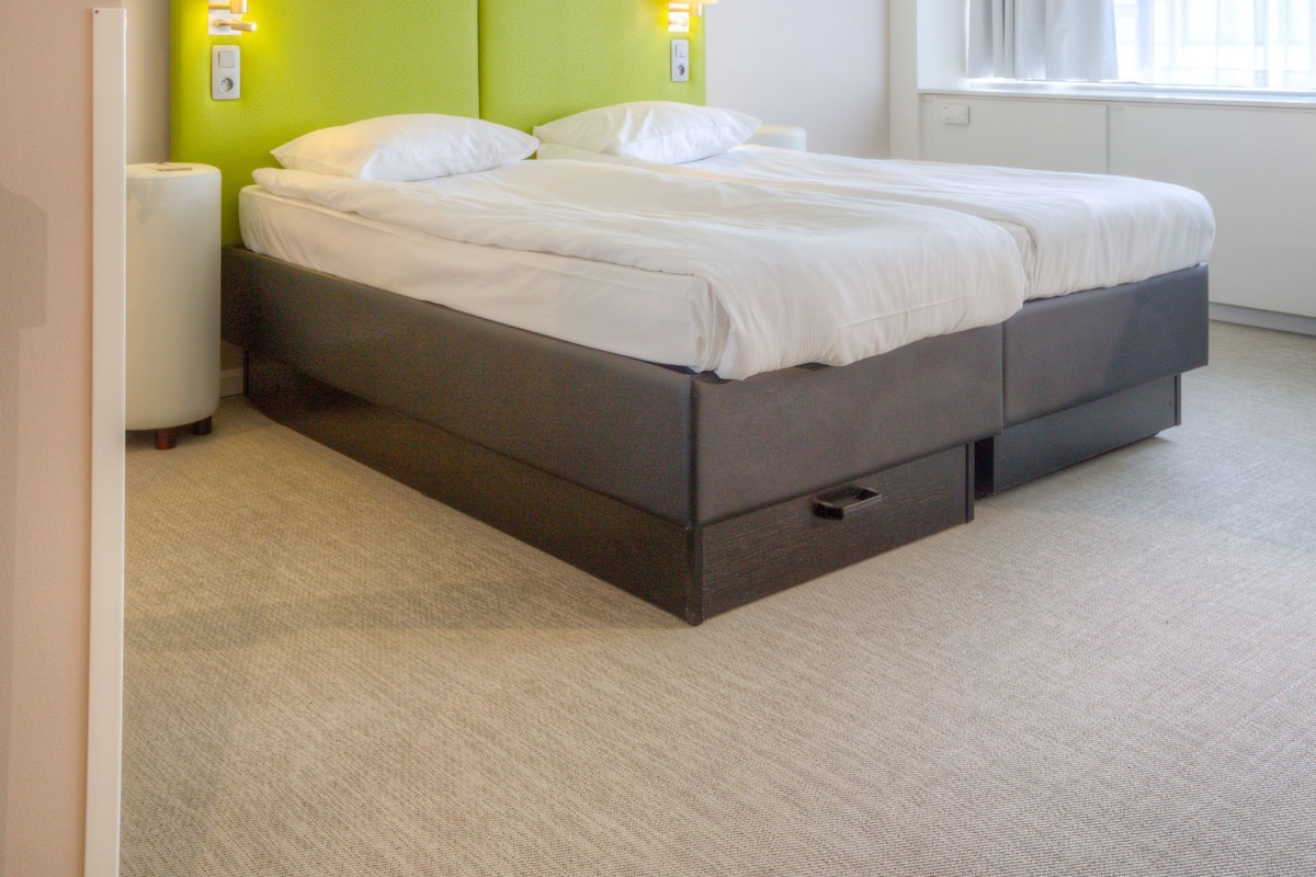 A hotel room with a bed, bedside lamps, a window, and a carpeted floor.