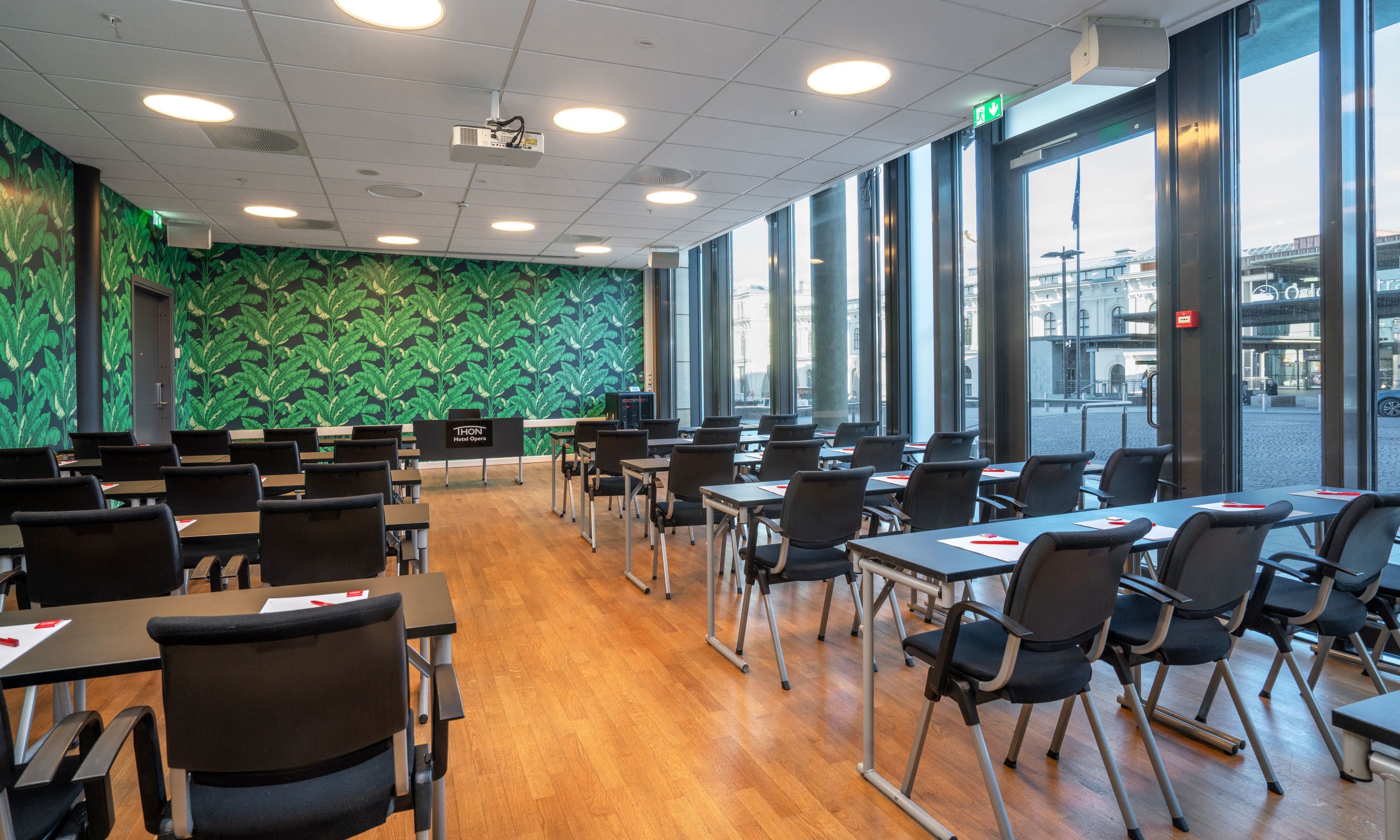 Ett konferensrum med en grön vägg dekorerad med ett lövmönster, stora fönster och en projektor i taket.