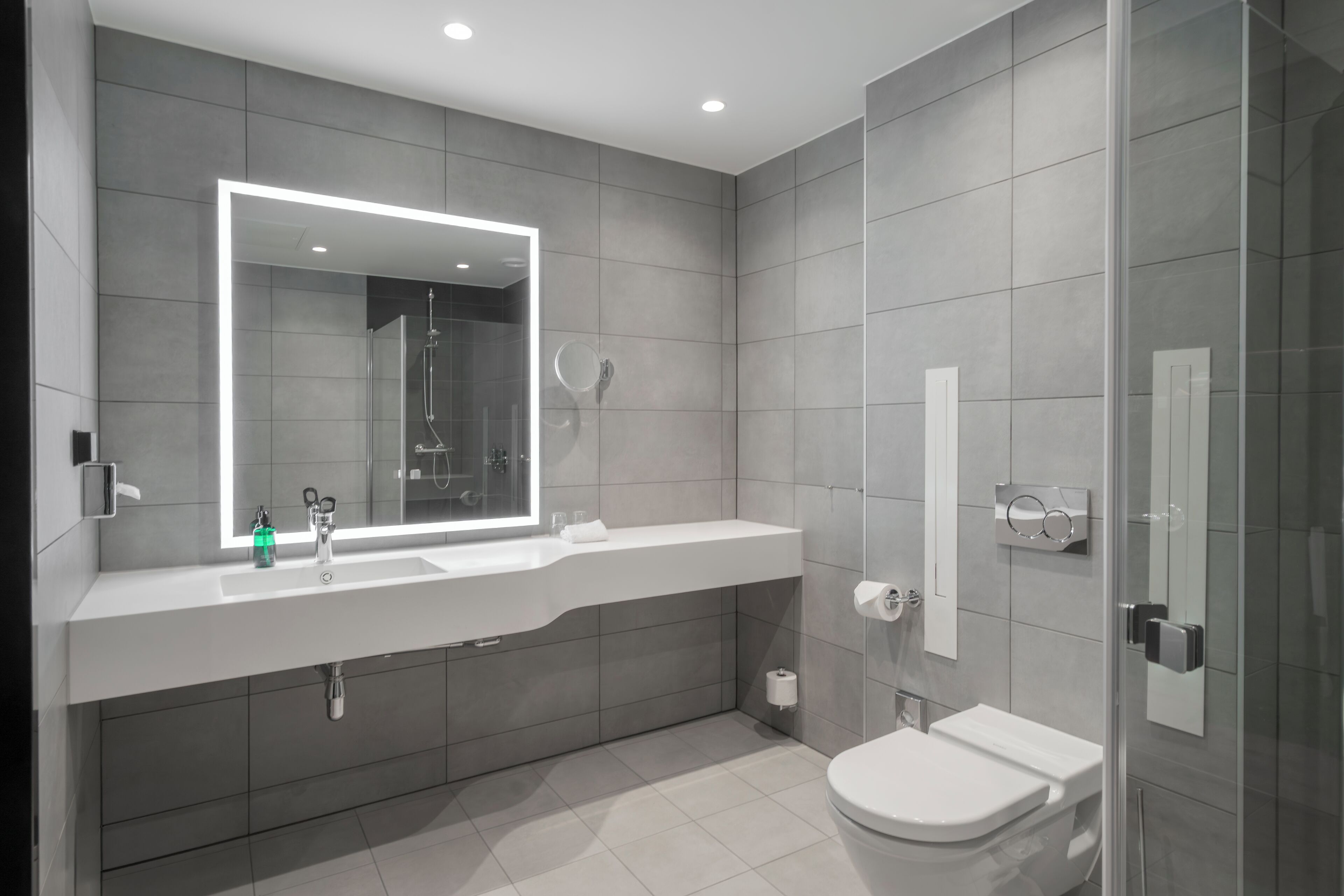 Un baño moderno con un espejo grande, una ducha, un inodoro y un lavabo.