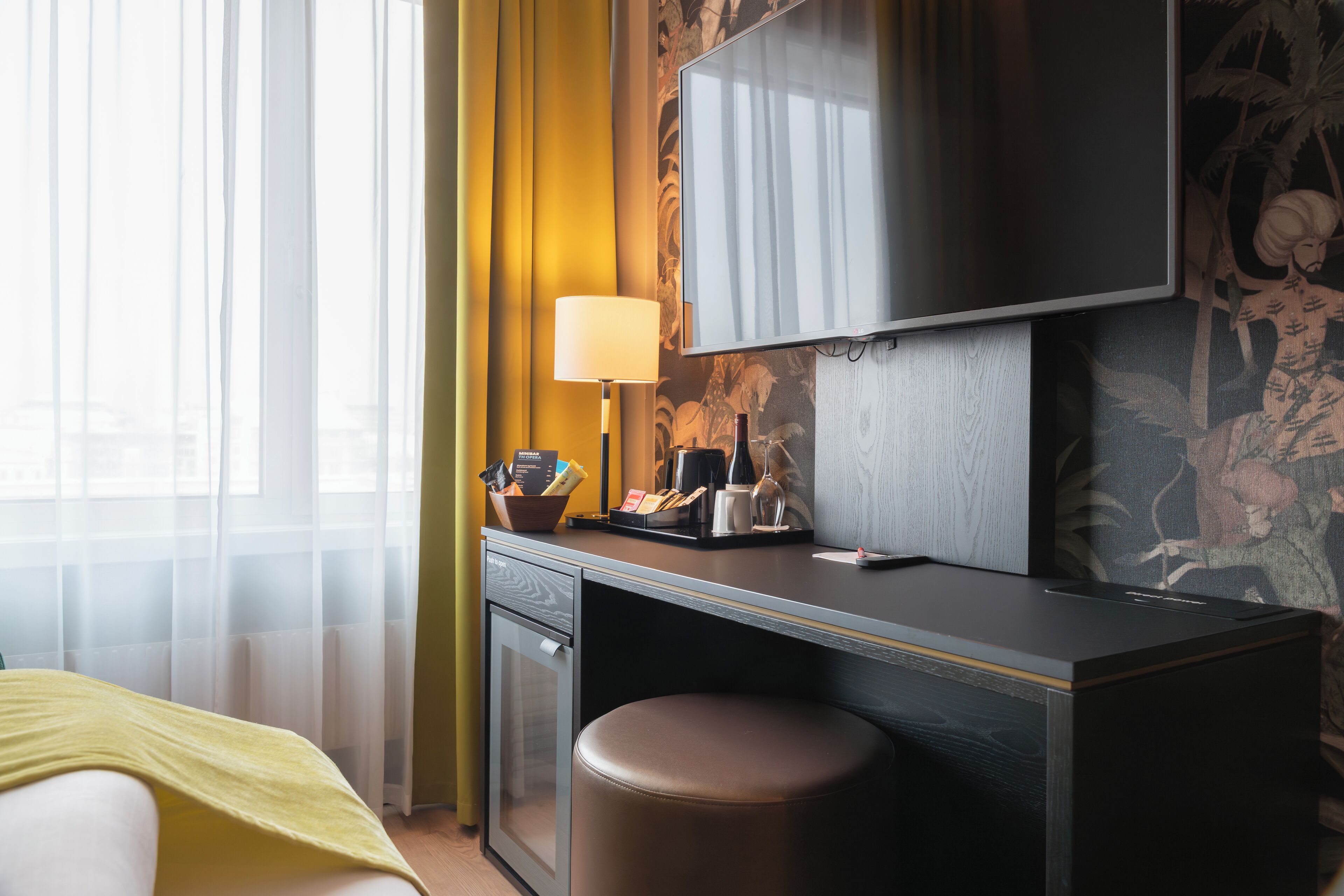 A hotel room with a bed, a desk with a lamp, a television, and a small cabinet.