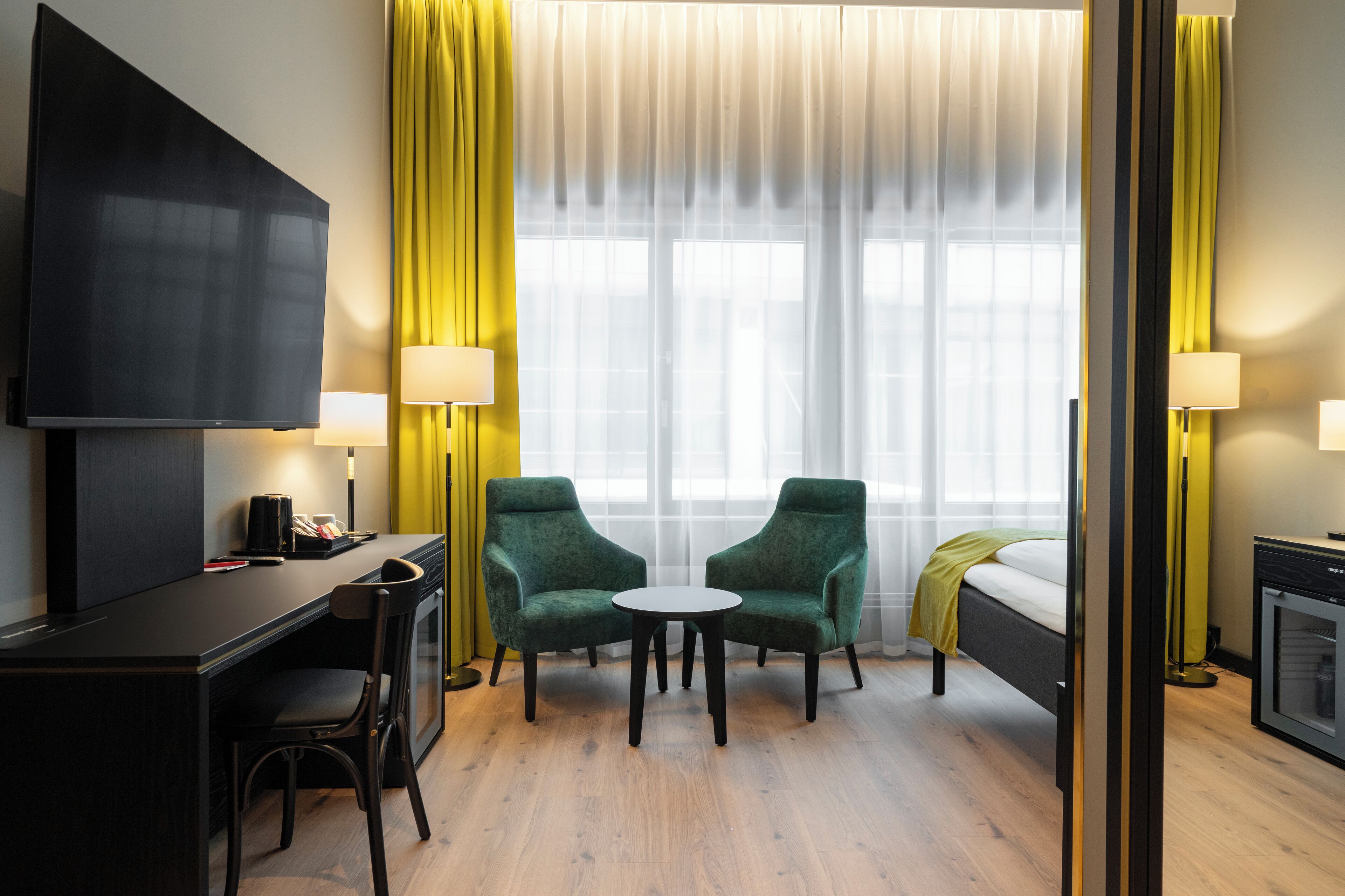 A hotel room with a bed, a desk with a chair, two armchairs, a small table, and a TV.