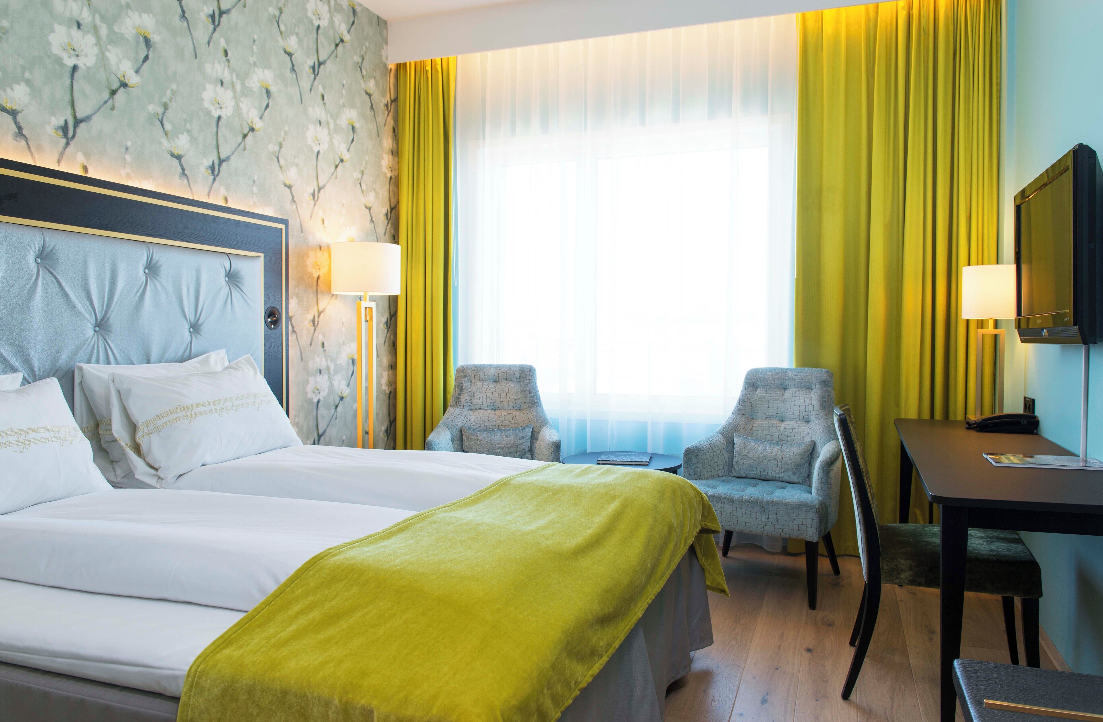 Habitación de hotel con una cama grande, dos sillones, un escritorio, un televisor y una ventana con cortinas.