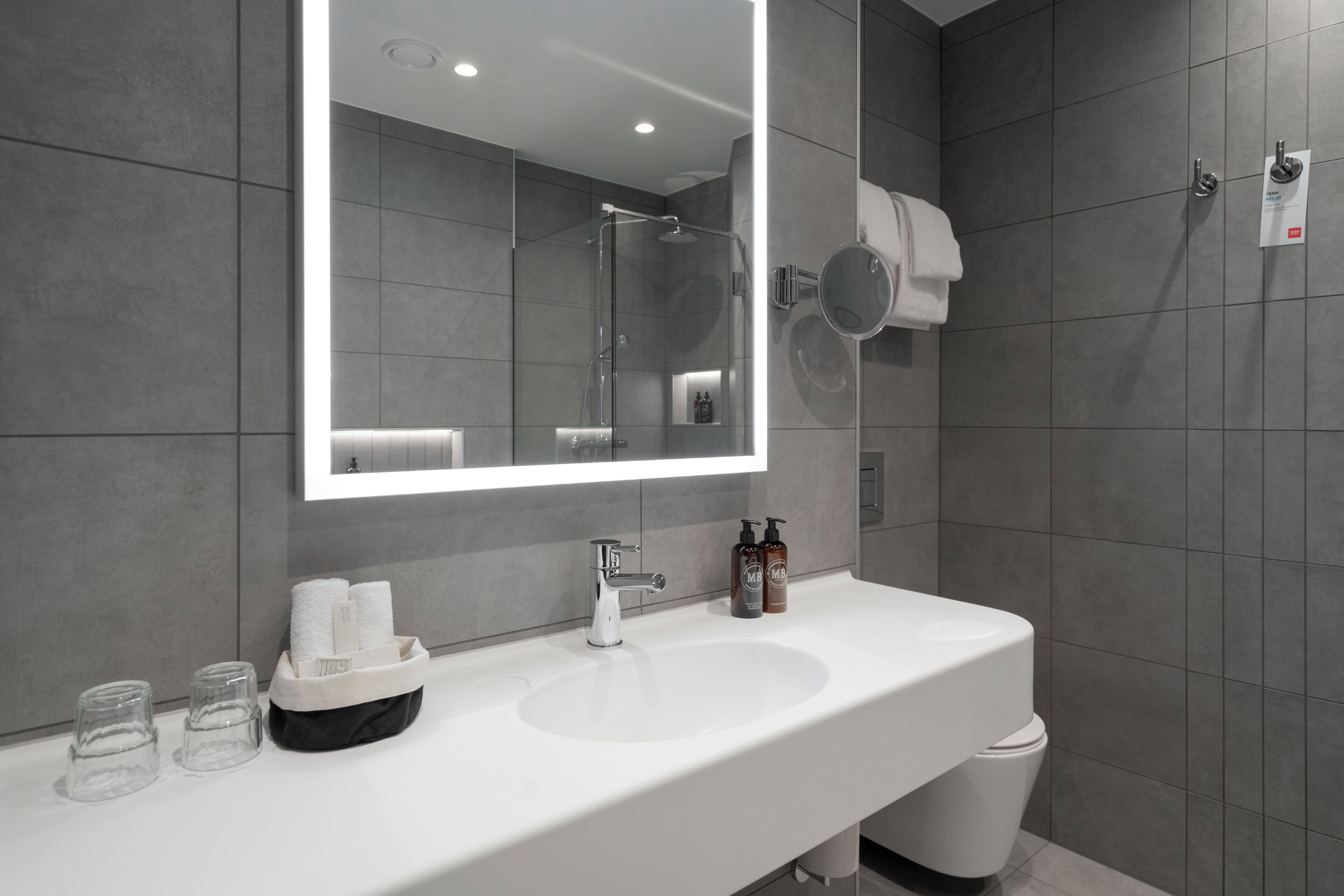 A modern bathroom with a large mirror, a white sink, and a shower area.