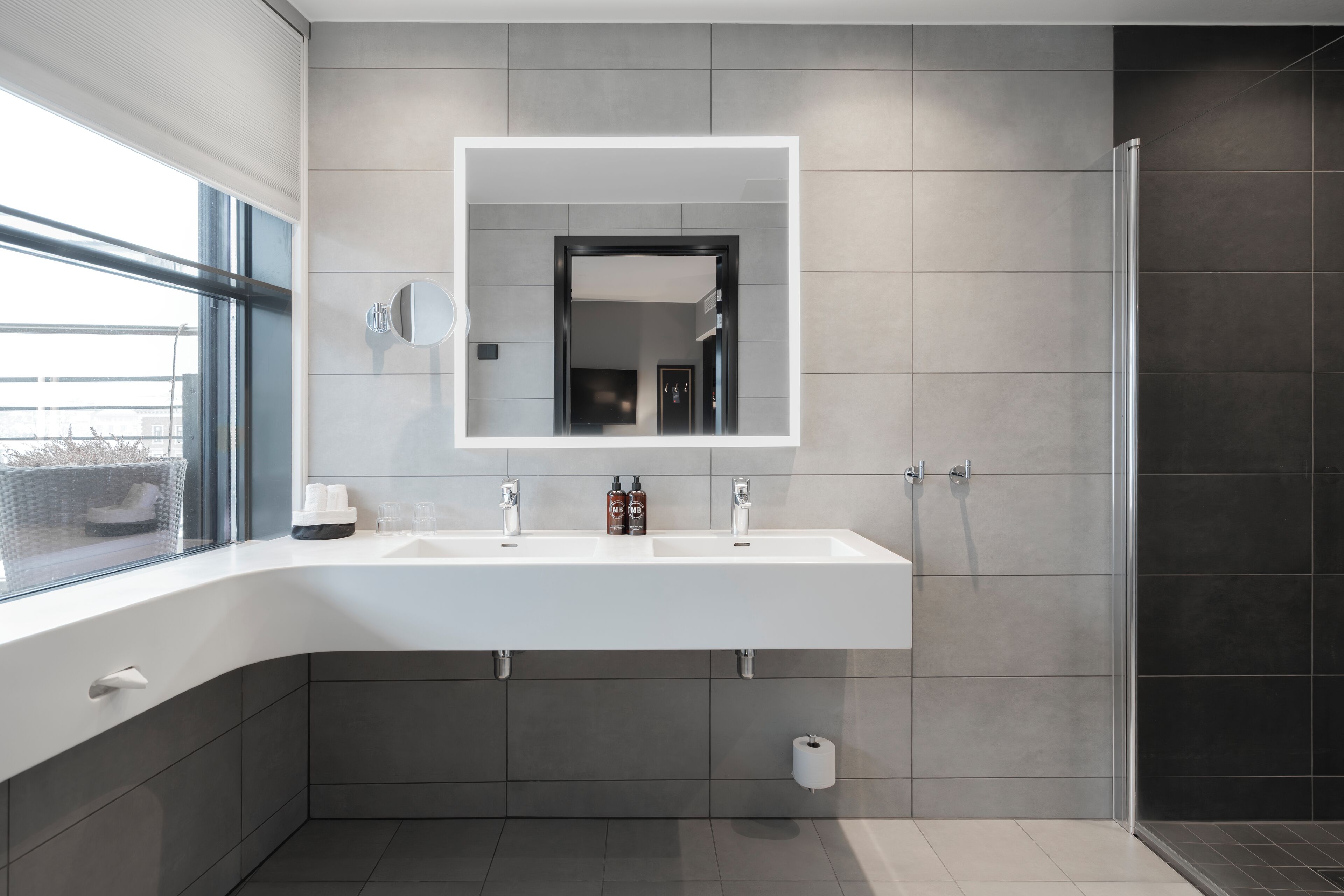 A modern bathroom with a large mirror, two sinks, and a shower area.