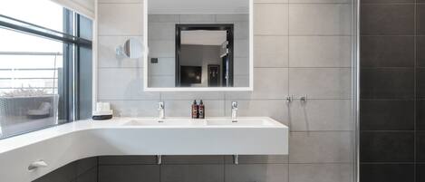 A modern bathroom with a large mirror, two sinks, and a shower area.