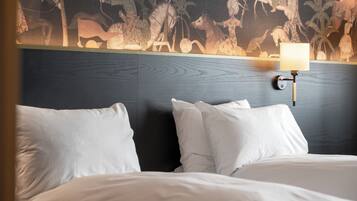 Ein Hotelzimmer mit Bett, weißen Kissen, einem dunklen Kopfteil und Wandgemälde.