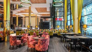 A modern restaurant interior with high ceilings, geometric patterned seating, and a large TV screen.