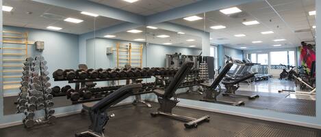 A gym with exercise equipment, mirrors, and a window.