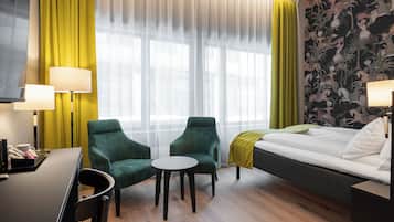 A hotel room with a bed, two chairs, a small table, a desk, and a TV.