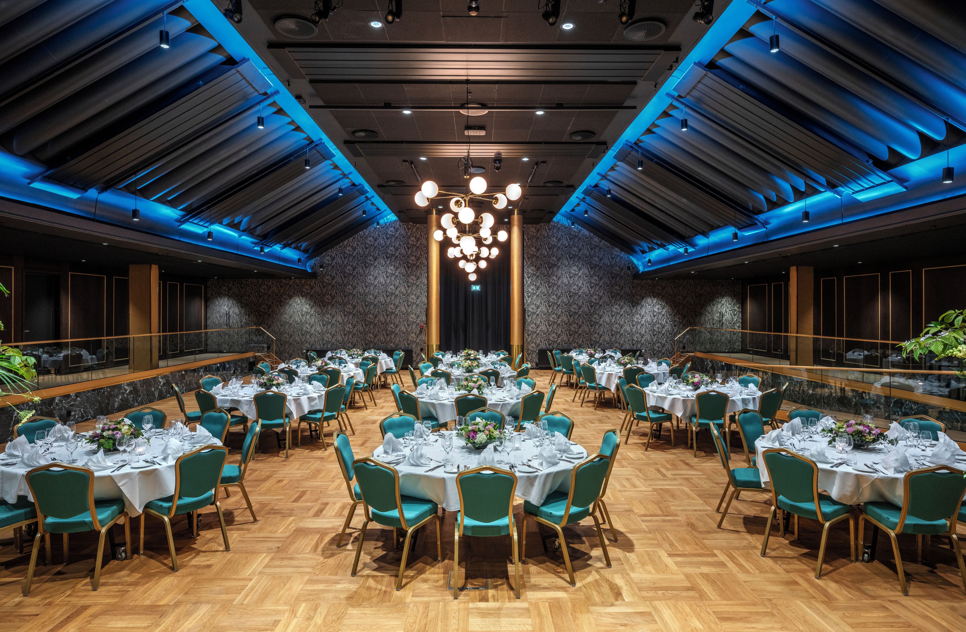 A spacious banquet hall with round tables set for dining, featuring teal chairs and white tablecloths.