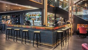 Een bar met een hoge toonbank, meerdere barkrukken en een divers aanbod aan flessen en glazen.