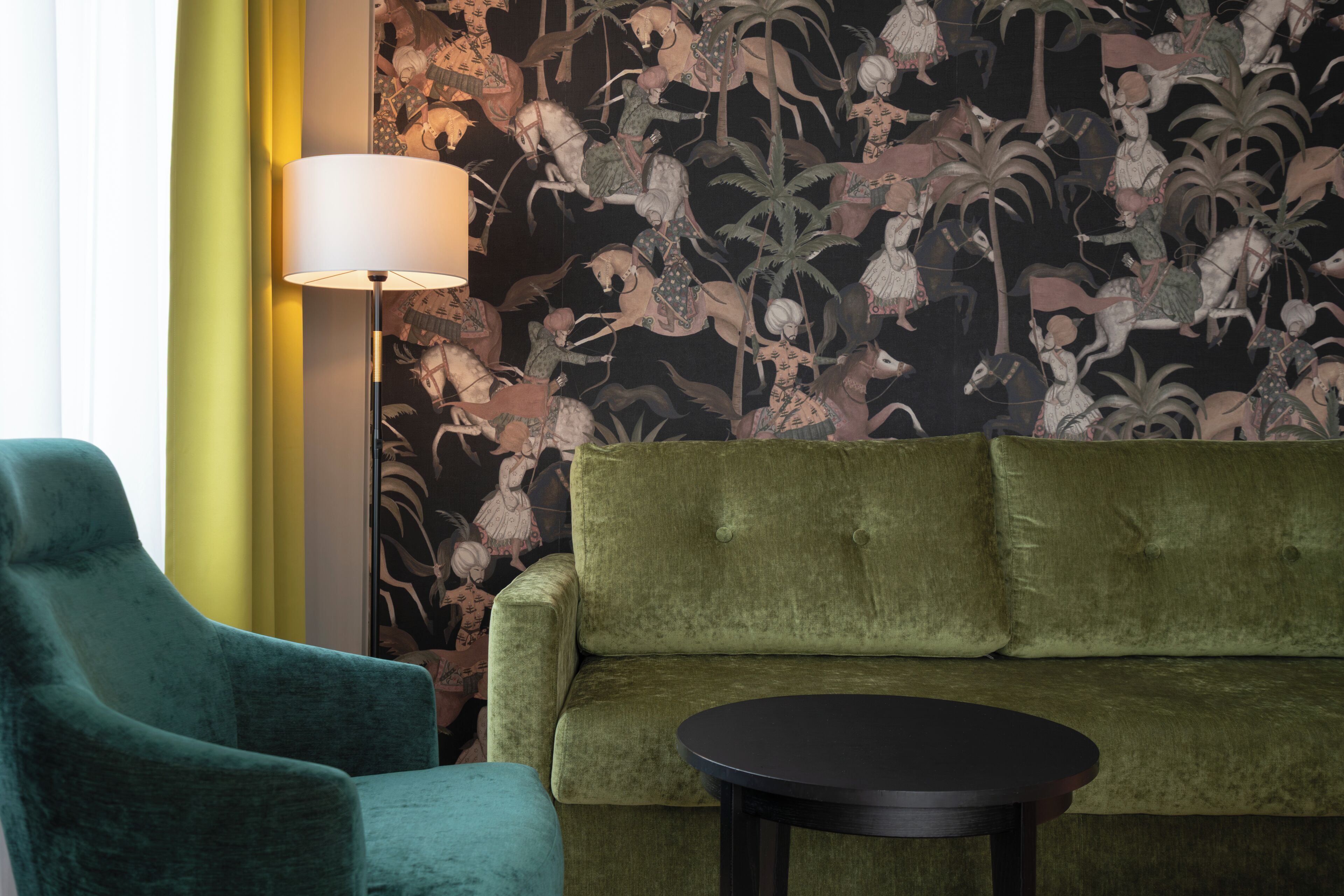 A room with a green sofa, a teal armchair, and a small round table.
