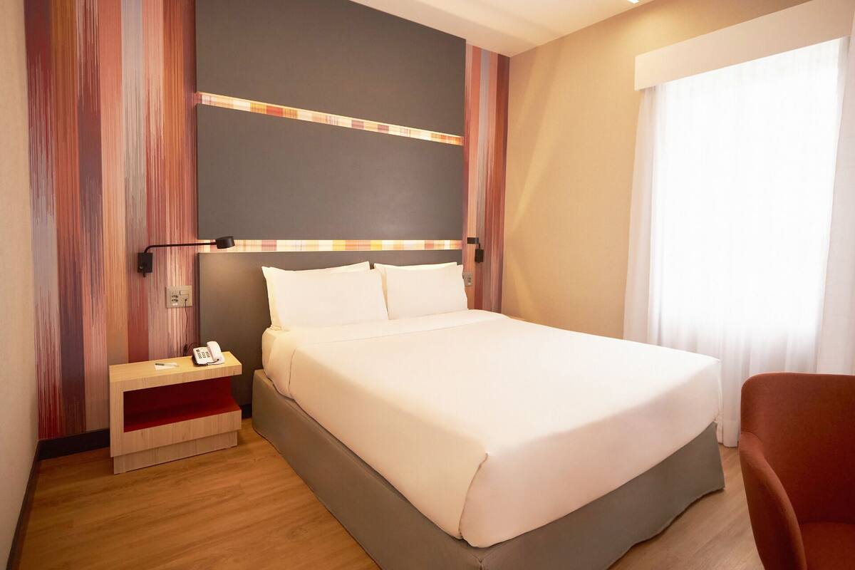 A hotel room with a bed, bedside table, and a chair.