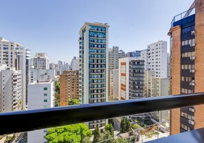 Un paisaje urbano con edificios altos modernos, una torre azul y beige destacada, y vista a través de la barandilla de un balcón.