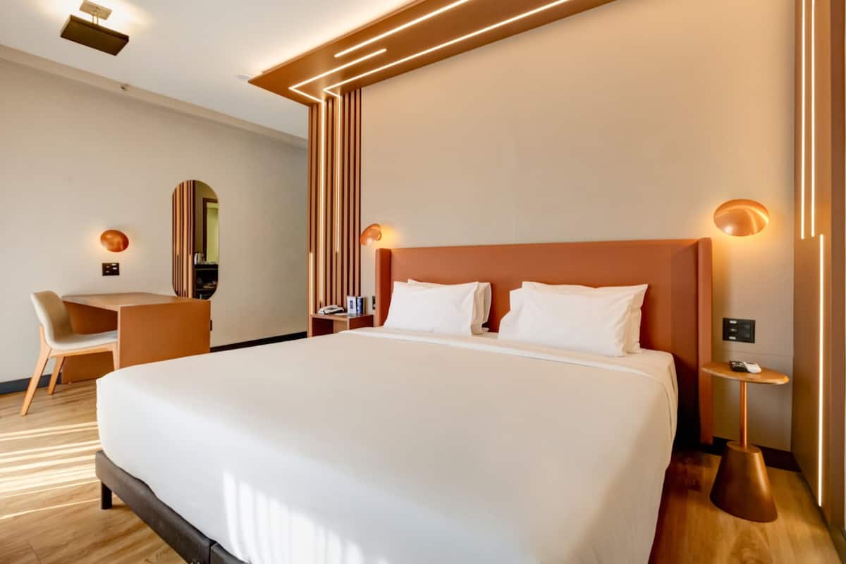 A modern hotel room with a large bed, a desk, and a chair.