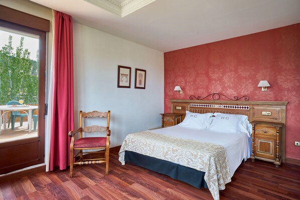 A bedroom with a wooden bed, a chair, a nightstand, and a window with curtains.