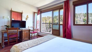 Habitación de hotel con una cama grande, un escritorio con televisor, una silla y vistas al exterior a través de amplios ventanales.