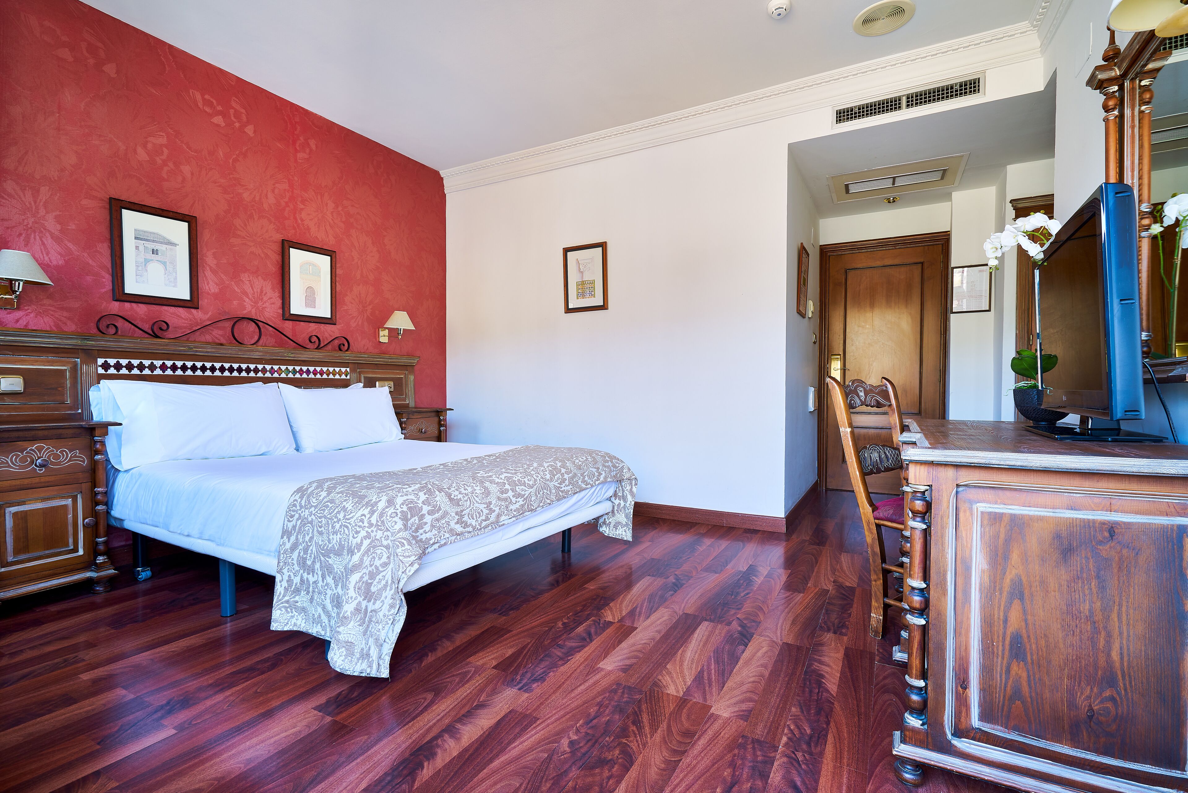 A hotel room with a wooden bed, a wooden dresser, and a red accent wall.