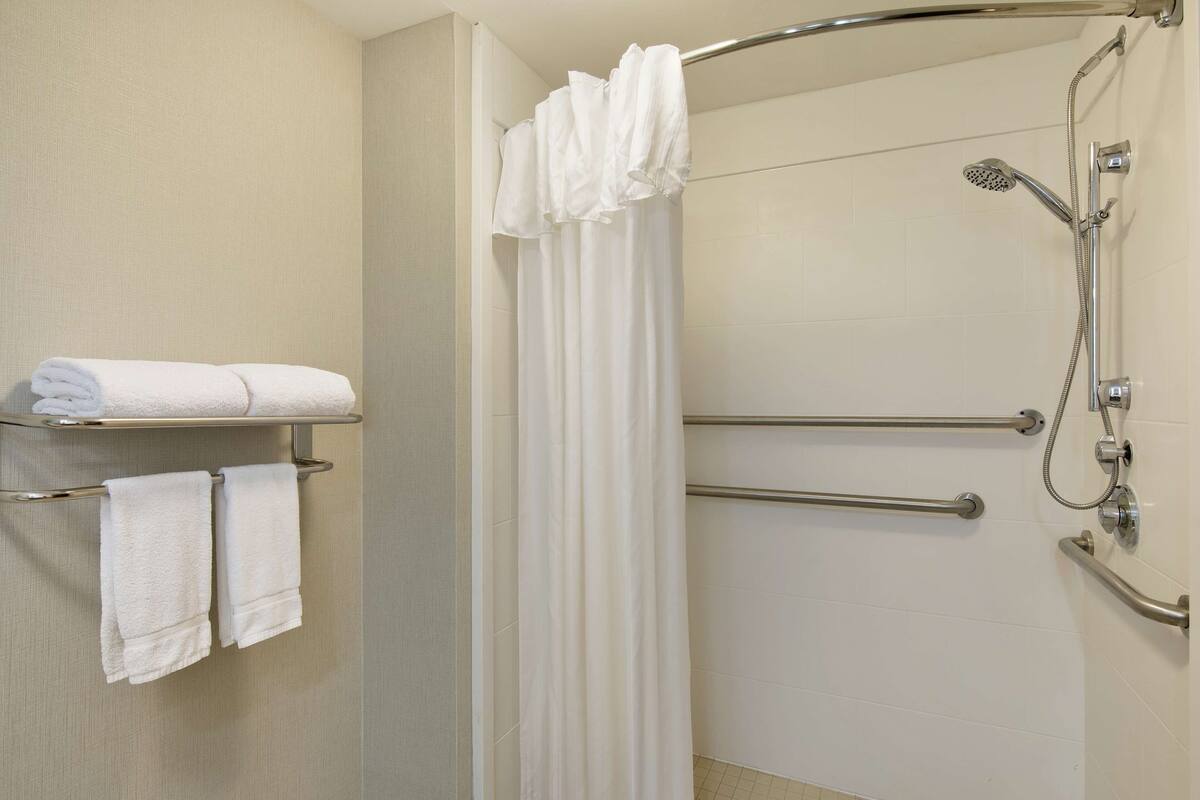 A shower area with a grab bar, a towel rack with towels, and a showerhead.